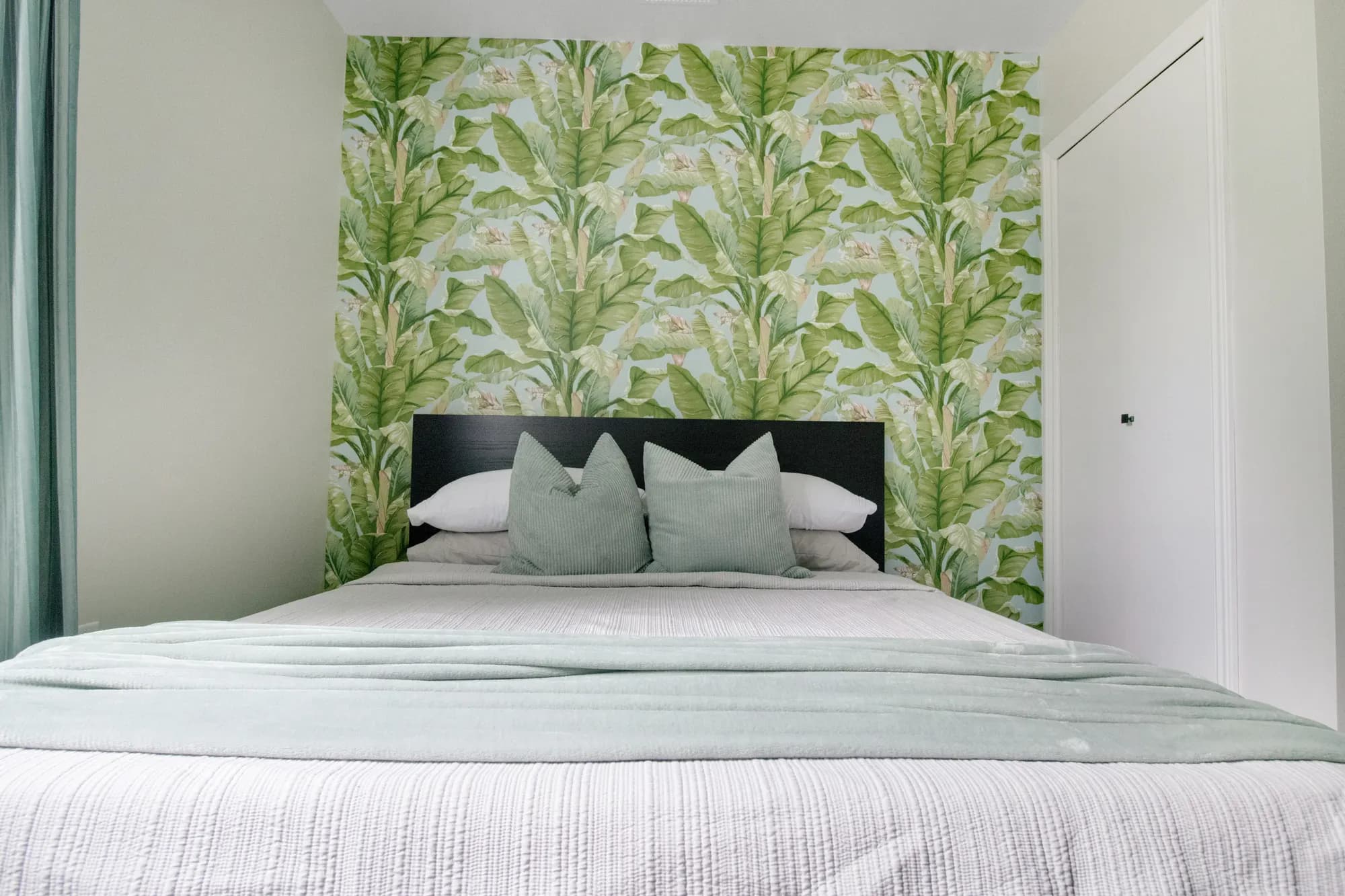 A bedroom with botanical wallpaper and a made bed